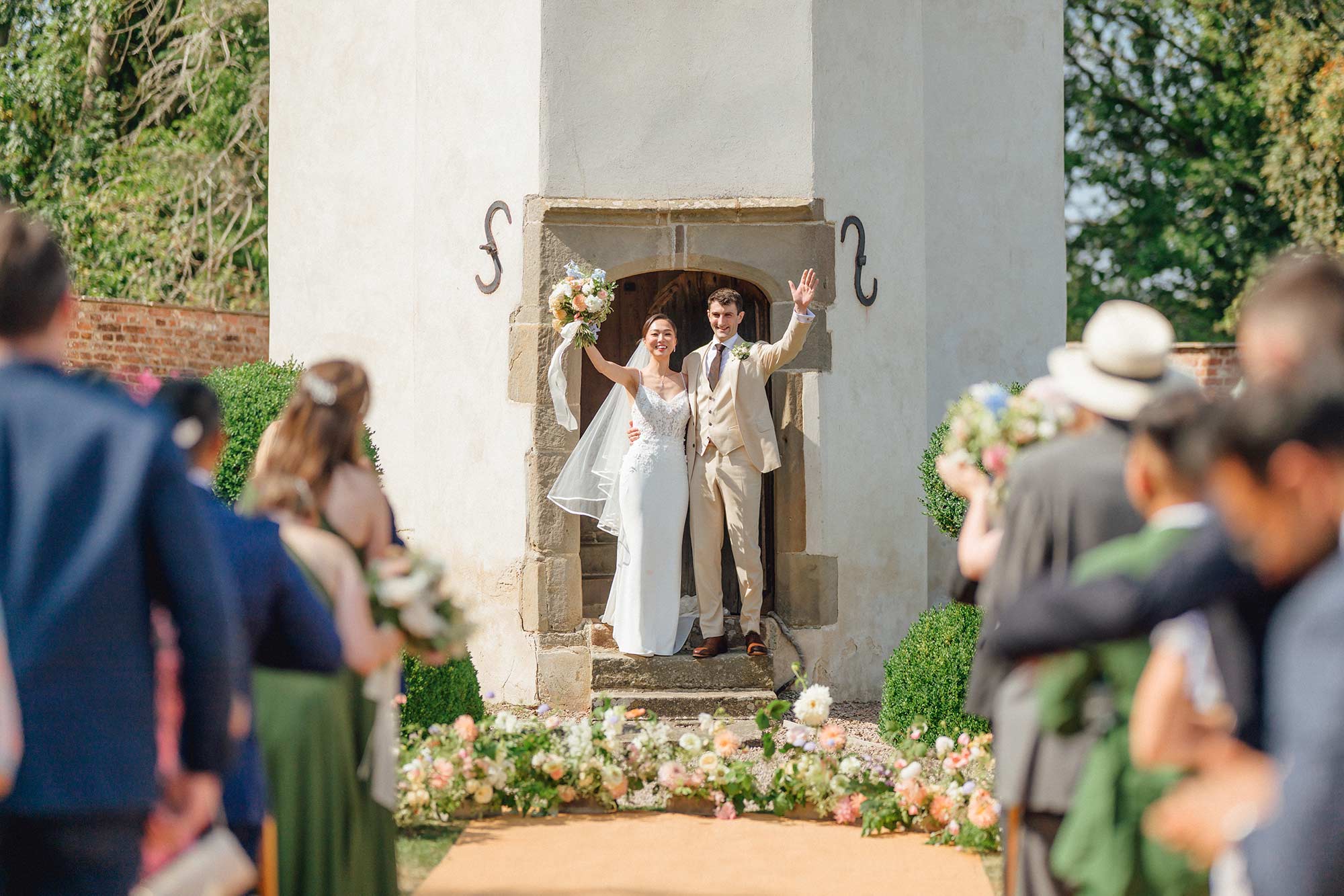 Bride-and-groom-wave-to-guests-as-they-emerge-from-Homme-House-Summerhouse-during-ceremony