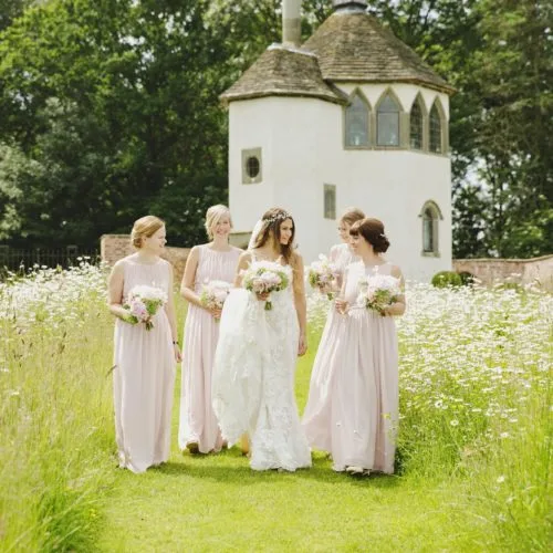 Bride and bridesmaids walking through wildflower meadow in the walled garden at Homme House