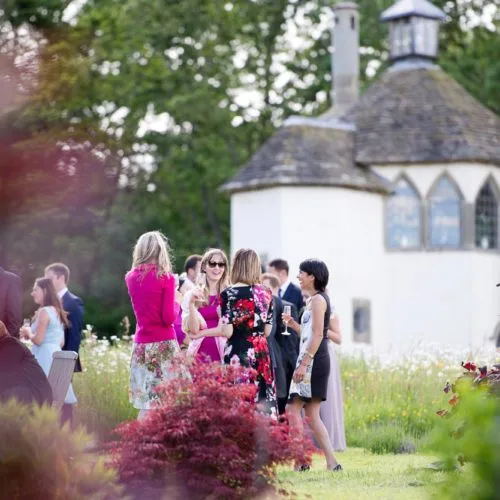 Wedding guests mingling near walled garden wildflower meadow at Homme House