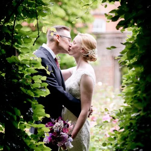Wedding couple kissing in front of the beech arch in the rose garden gate at Homme House