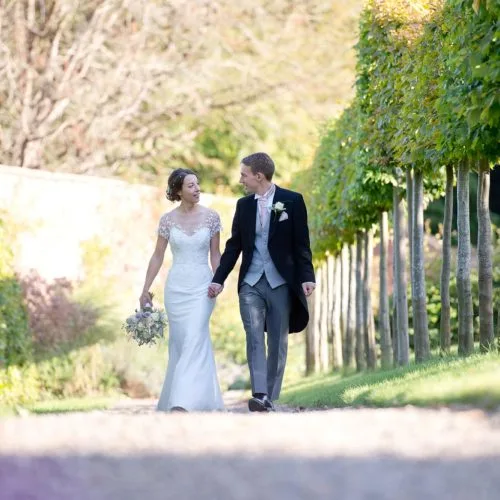 Bride and groom walking pleached walkway in the walled garden at Homme House