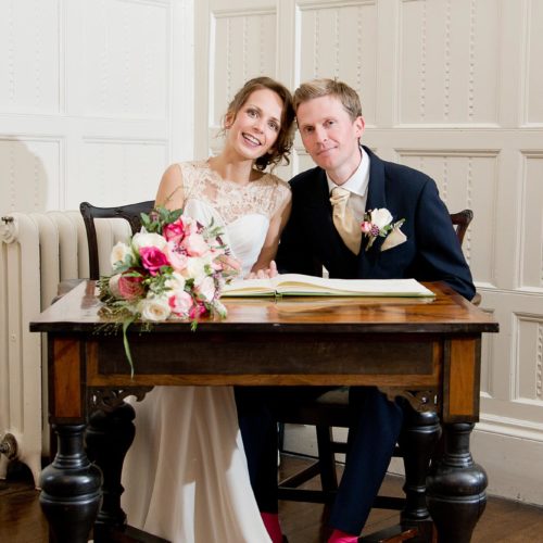 A bride and groom sign the register during a Panelled Room ceremony at Homme House