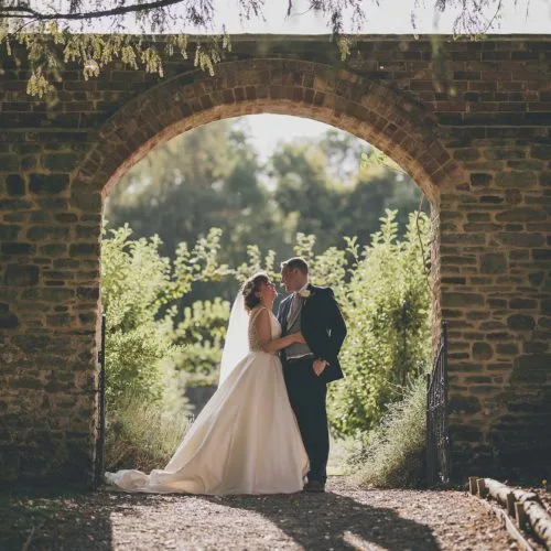 Bride and groom embracing under the archway entrance to the Walled Garden at Homme House