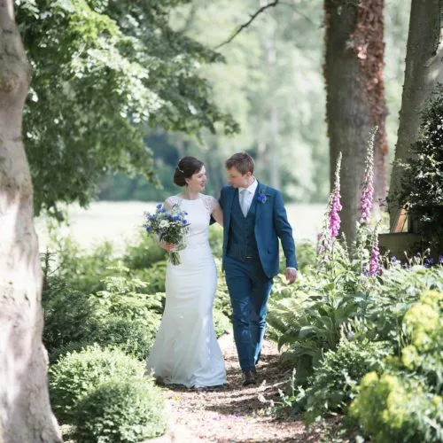 A bride and groom walk through a woodland glade at Homme House