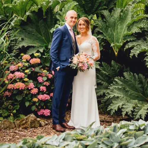 A wedding couple pose in front of huge gunnera at Homme House