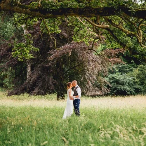 A wedding couple kiss in Homme House\'s historic parkland