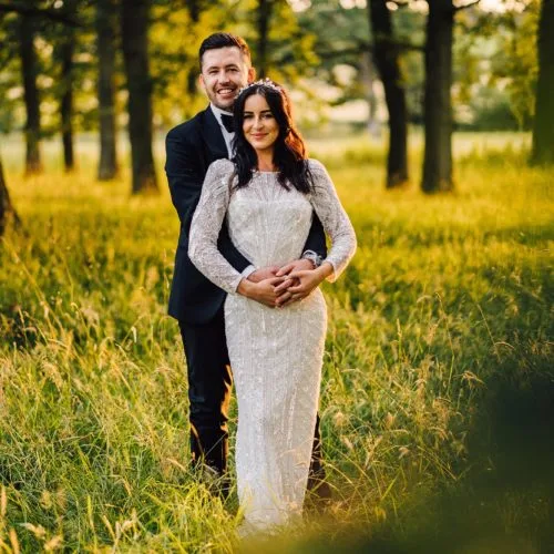 A bride and groom pose in a parkland woodland copse