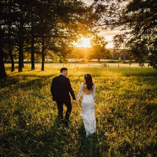 A wedding couple walk in Homme House\'s parkland grass in evening sunshine