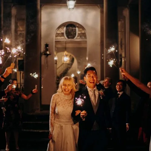 Bride, groom and guests with sparklers outside the front of Homme House in the evening