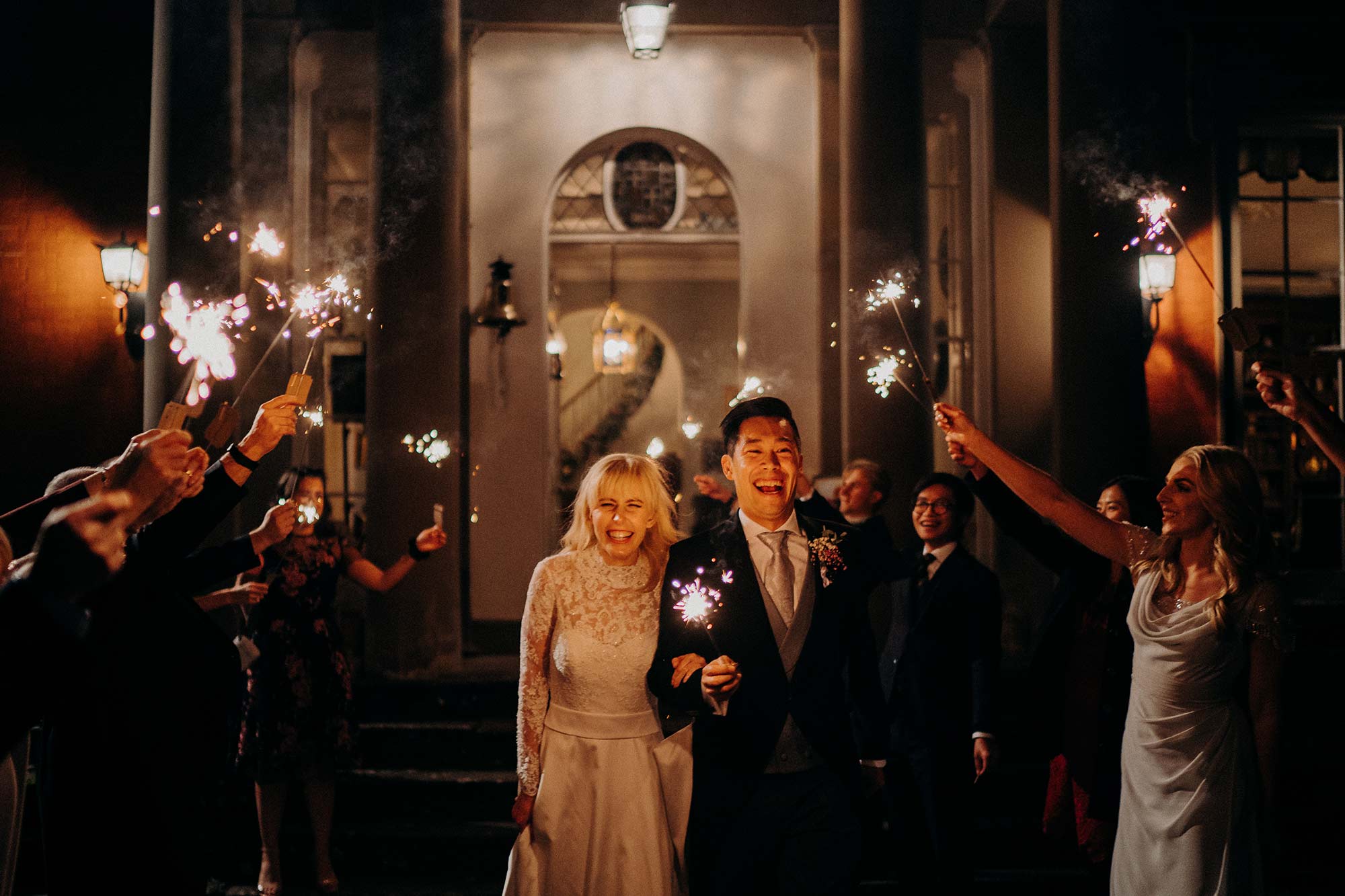 Bride, groom and guests with sparklers outside the front of Homme House in the evening