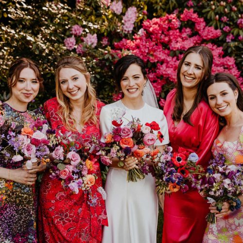 Bride-and-bridesmaids-in-colourful-dresses-in-front-of-Homme-House-rhododendrons