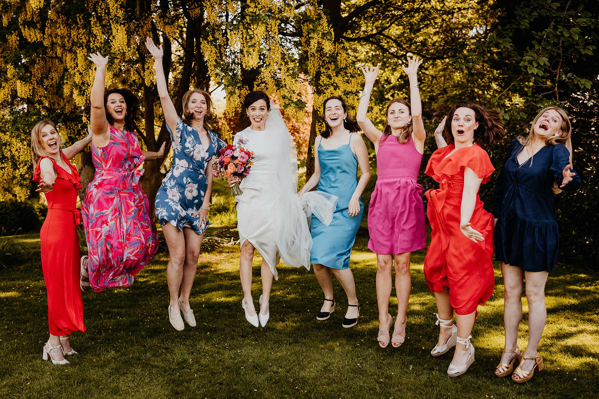 Bride-and-bridesmaids-jumping-in-group-photo-under-Homme-House-laburnum