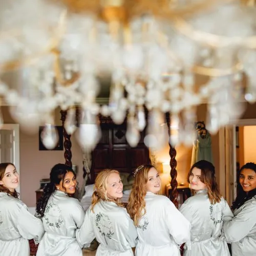 Bride-and-bridesmaids-pose-in-dressing-gowns-under-chandelier-in-bridal-bedroom