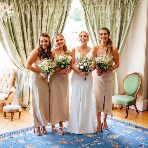 Bride-and-bridesmaids-pose-with-flowers-in-front-of-Homme-House-Main-Suite-windows