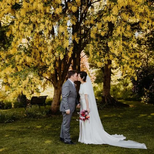 Bride-and-groom-kiss-under-Homme-House-laburnum