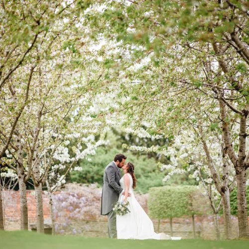 Bride-and-groom-kiss-under-walled-garden-blossom-at-Homme-House
