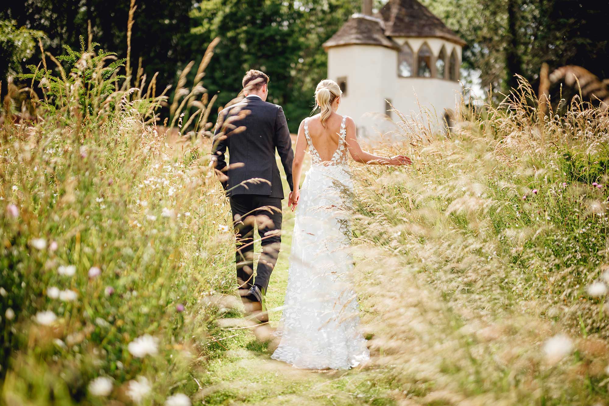 Bride-and-groom-walk-through-wildflower-meadow-at-Homme-House