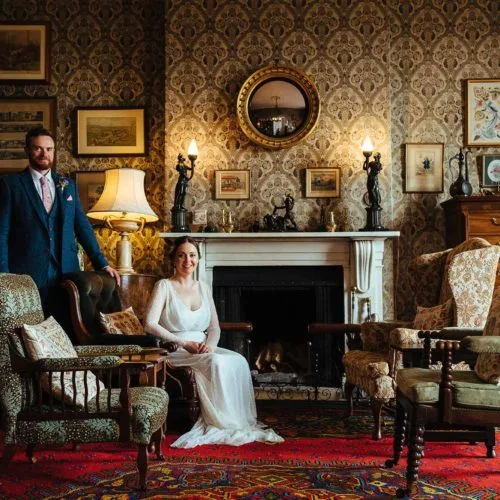 Couple-sitting-and-standing-close-to-Homme-House-Library-fireplace