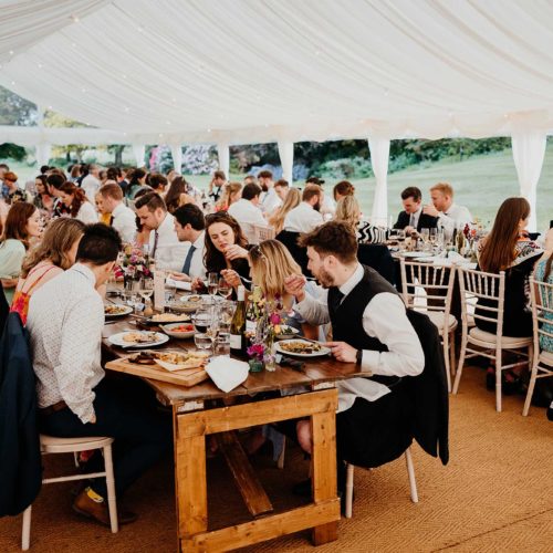 Guests-eating-at-marquee-banqueting-tables-at-wedding-at-Homme-House