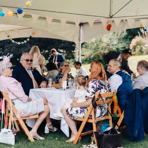 Guests-sitting-under-canopy-cover-on-lawn-at-wedding