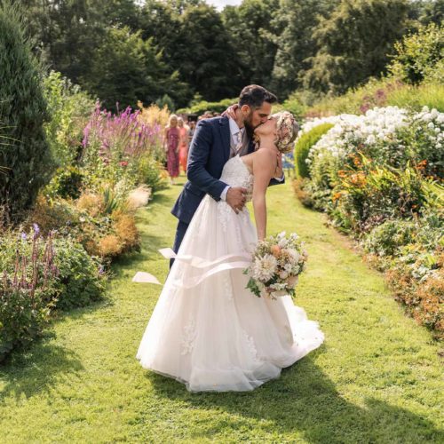 Bride-and-groom-kiss-on-long-borders-in-Homme-House-walled-garden