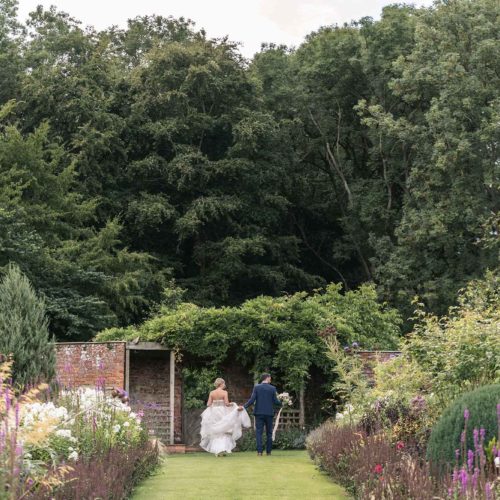 Bride-and-groom-walking-away-at-top-of-long-Homme-House-herbaceous-borders
