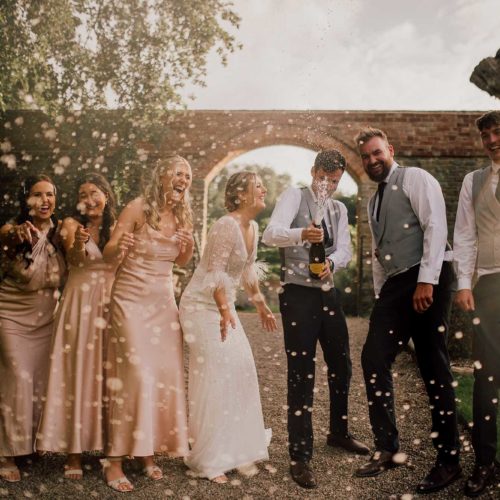 Bride-groom-and-bridal-party-spray-champagne-in-garden-at-Homme-House