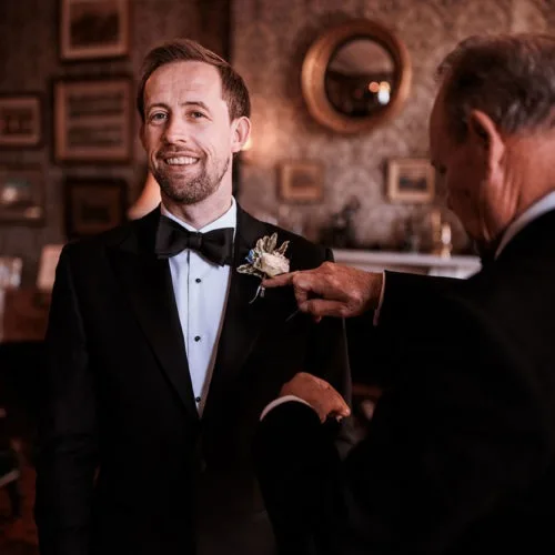 Groom-in-black-tie-having-buttonhole-pinned