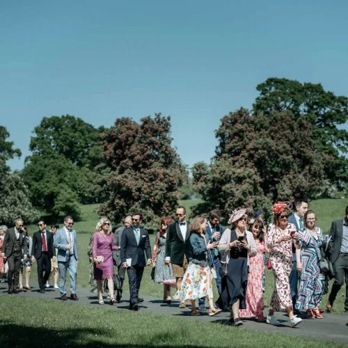 Wedding-guests-walk-back-from-church-through-Homme-House-parkland
